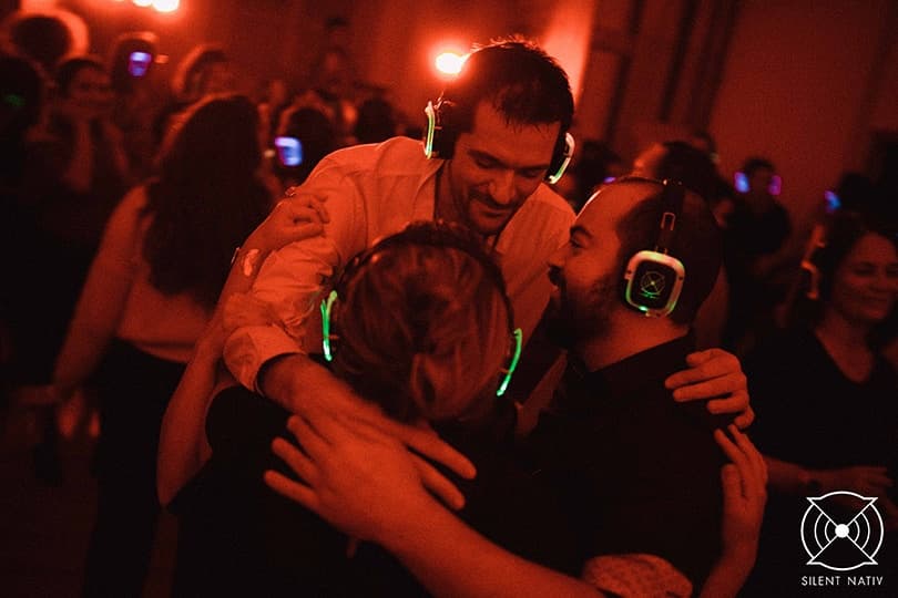 Amis se prenant dans les bras lors d’une silent party, casques lumineux